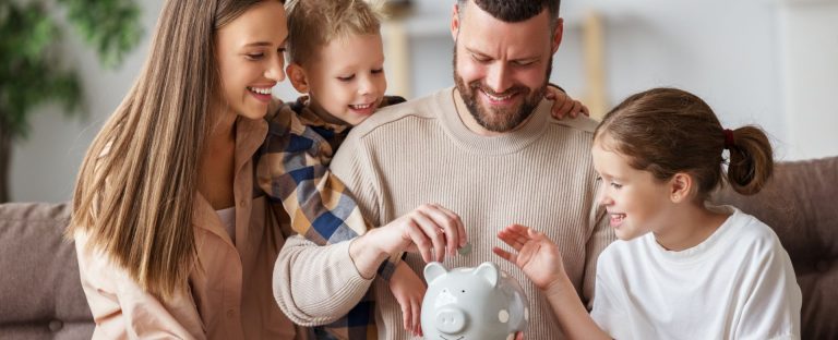 L’immagine che accompagna l’approfondimento sul Museo del Risparmio ritrae una famiglia sorridente composta da papà, mamma e due bambini seduti insieme vicini su un divano e intenti a seguire l'atto del papà di introdurre una moneta in un salvadanaio dalla classica forma di porcellino