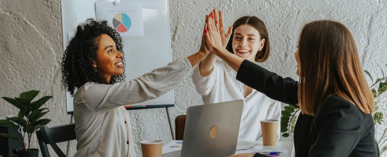 L’immagine che accompagna la News sulla sesta edizione del programma “Imprese Vincenti” di Intesa Sanpaolo che premia le PMI eccellenti e le aiuta a crescere in Italia e all’estero, ritrae tre colleghe sedute intorno a una scrivania, mentre "battono il cinque" in segno di accordo e successo incrociando le mani sopra il pc appoggiato al centro del tavolo